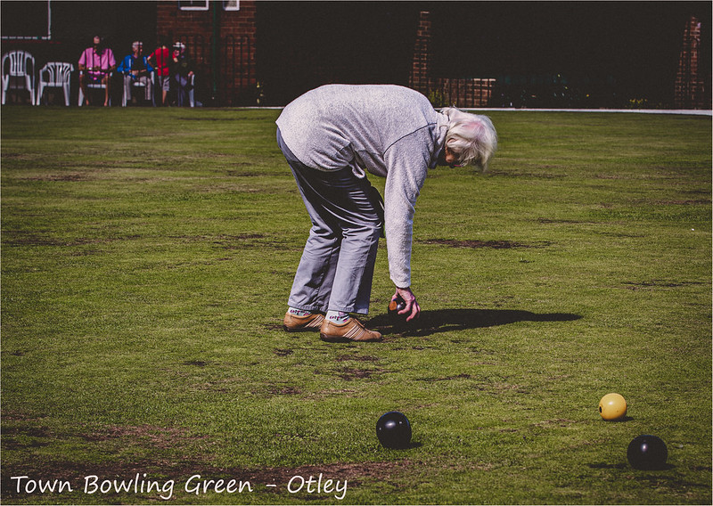 An older women bending down on a bowling green while playing Crown Green Bowls in the town of Otley